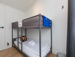 Una cama litera con dosel gris y una bolsa azul encima.