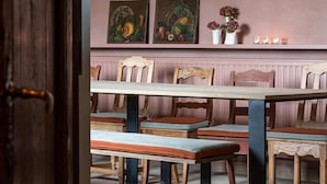 A dining area with wooden tables and chairs, a pink wall with artwork and candles, and a wooden door. - Stately 16-person Manor Farm in South Limburg (Schimmert)