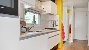 Cozinha moderna com armários brancos, fogão a gás e janela com vista para um jardim.