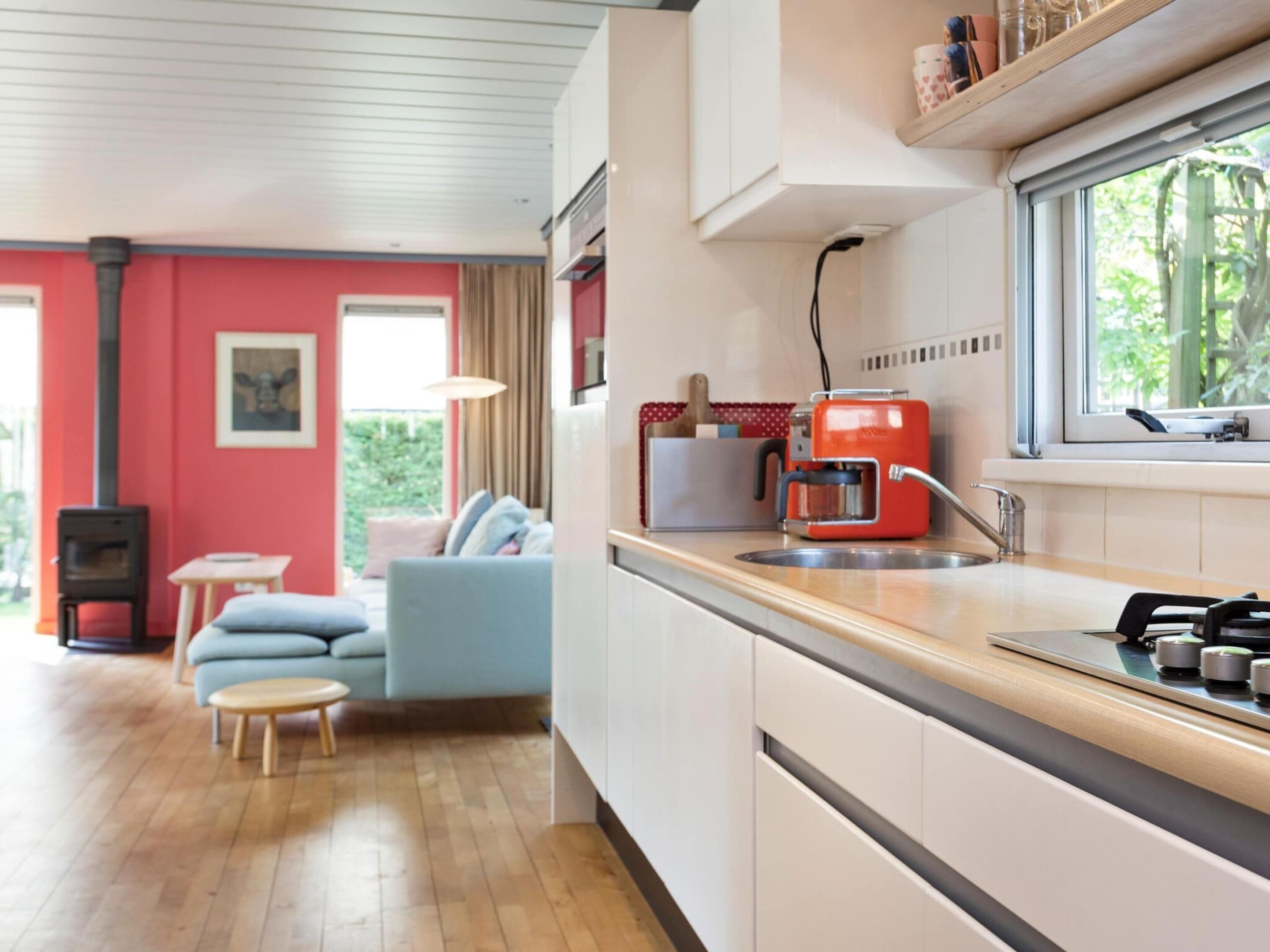 A modern kitchen with a red appliance, a window, and a view of greenery.