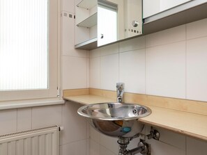 A bathroom with a stainless steel sink, a mirror above it, and a window with blinds.