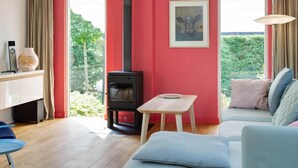 Uma sala de estar moderna com parede vermelha, lareira a lenha preta, sofá azul e pequena mesa de madeira.