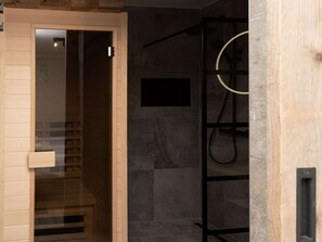 Bany modern amb mampara de vidre, porta de fusta i penjador de tovalloles negre.