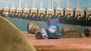 A table with a rolled towel and a bag, a rocky shoreline, and a large industrial structure with multiple chimneys in the background. - Apartment on Tholen by Oosterschelde Estuary (Scherpenisse)
