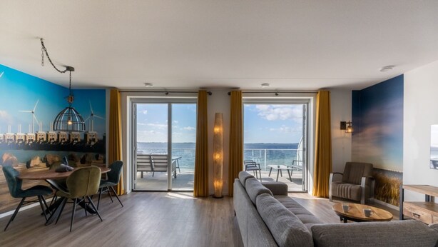 A modern living room with a sofa, dining table, chairs, and a view of the sea through large windows. - Apartment on Tholen by Oosterschelde Estuary (Scherpenisse)