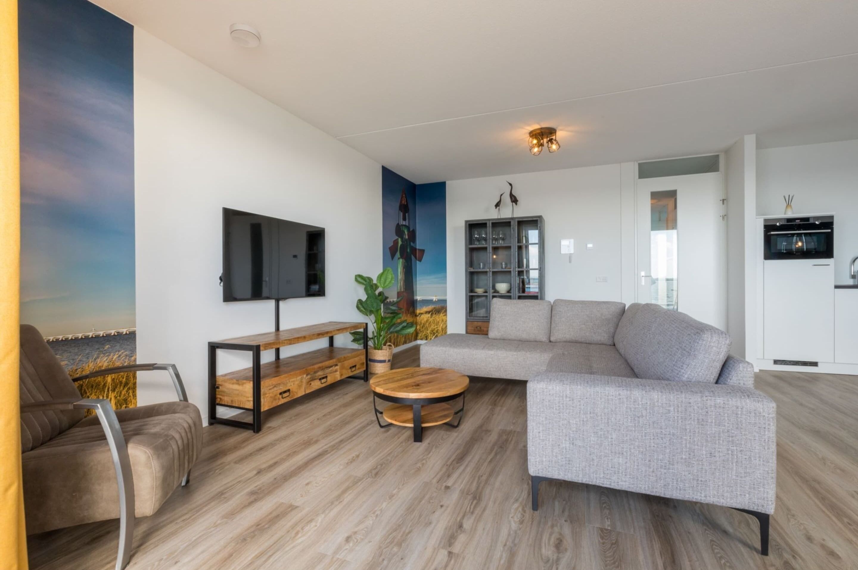 A modern living room with a sectional sofa, a coffee table, a TV mounted on the wall, and a bookshelf.