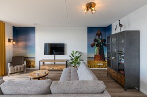 A modern living room with a sofa, coffee table, TV, and artwork on the walls.