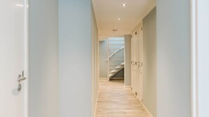 A narrow hallway with light-colored walls and wooden flooring, leading to a staircase. - Luxurious 16-person Villa With Swimming Pool Sauna Outdoor Kitchen With BBQ (Ouddorp)
