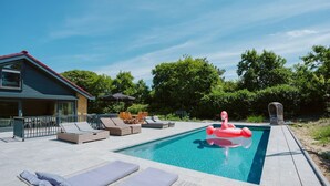 A swimming pool with lounge chairs and a flamingo float. - Luxurious 16-person Villa With Swimming Pool Sauna Outdoor Kitchen With BBQ (Ouddorp)