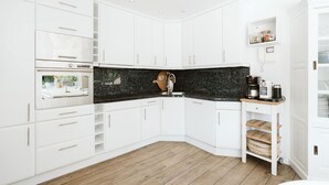 A modern kitchen with white cabinetry, a black granite countertop, and a wooden floor. - Luxurious 16-person Villa With Swimming Pool Sauna Outdoor Kitchen With BBQ (Ouddorp)