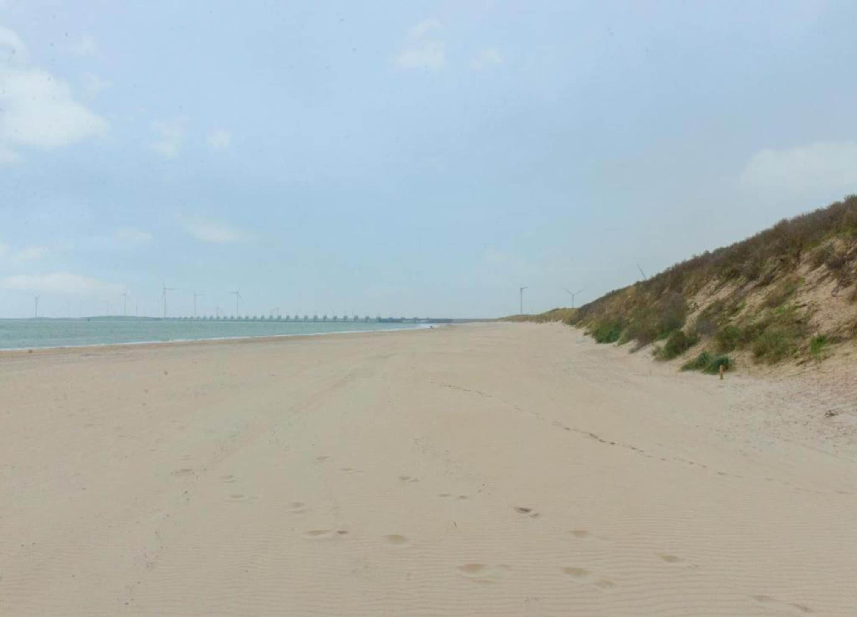 A wide sandy beach with a gentle slope on the right, leading to a grassy hill.