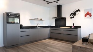 Une cuisine moderne avec des meubles gris, un plan de travail noir et un plancher en bois.