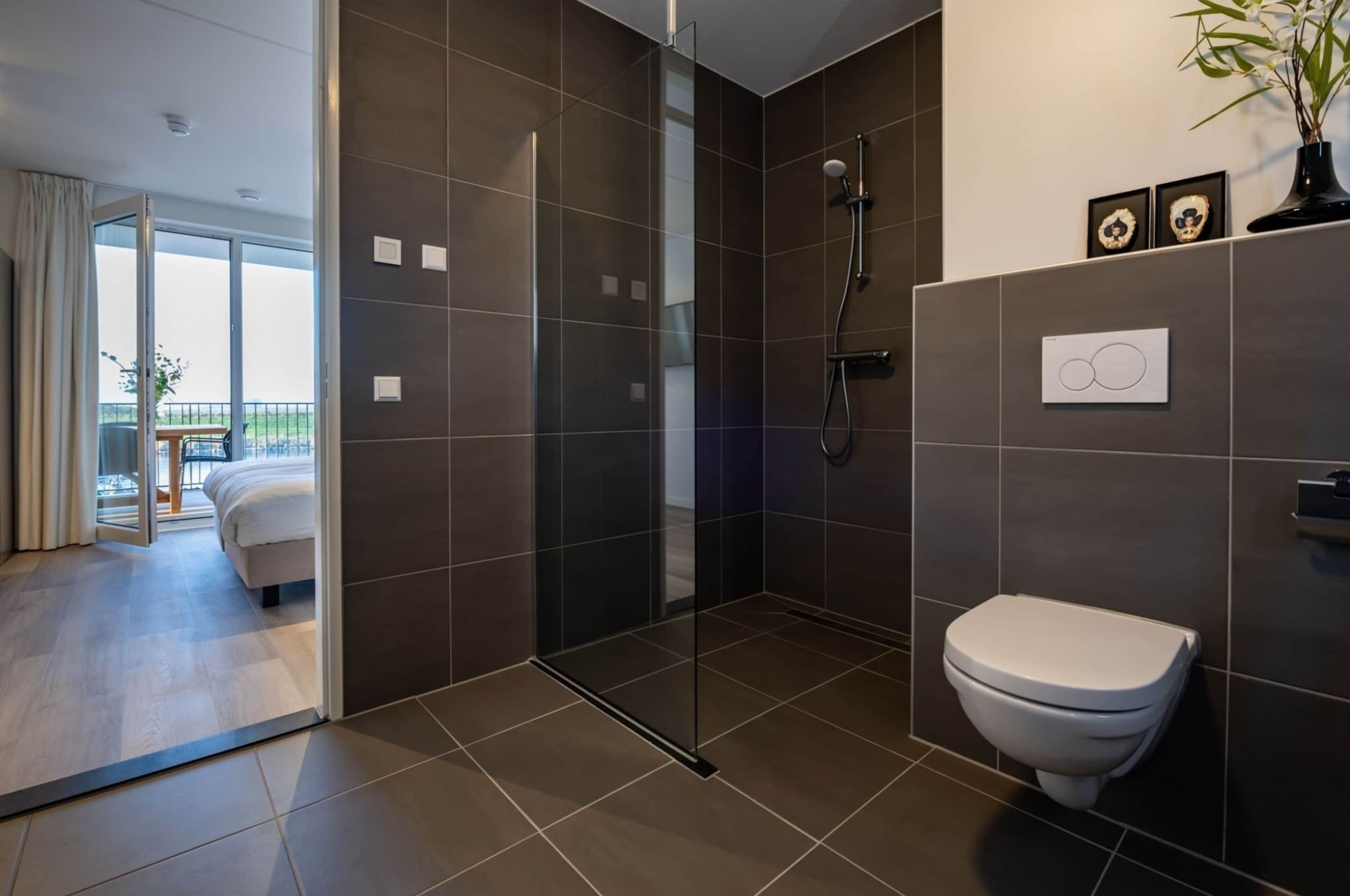 A modern bathroom with a glass-enclosed shower, a toilet, and a large window offering a view of a balcony.