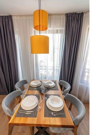 A dining area with a wooden table set for four, two pendant lights, and grey upholstered chairs. - Pomorie Seaside Apartments (Pomorie)