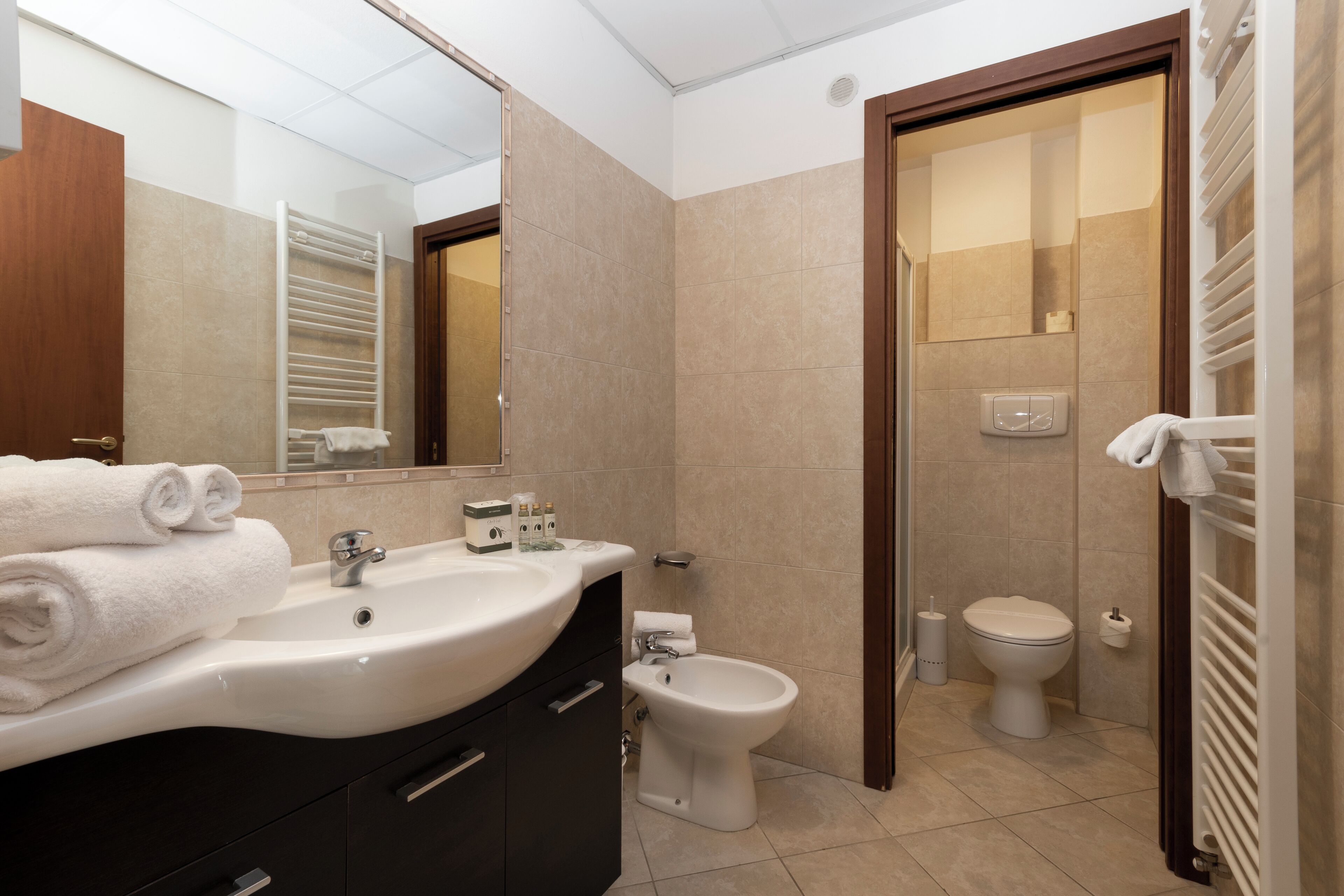 A modern bathroom with a sink, mirror, towel rack, toilet, bidet, and a shower area.
