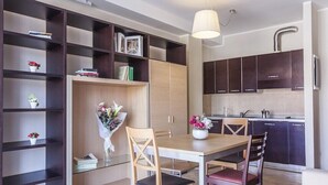 Una cocina moderna con armarios oscuros, una mesa de comedor con sillas y una estantería empotrada con objetos decorativos.