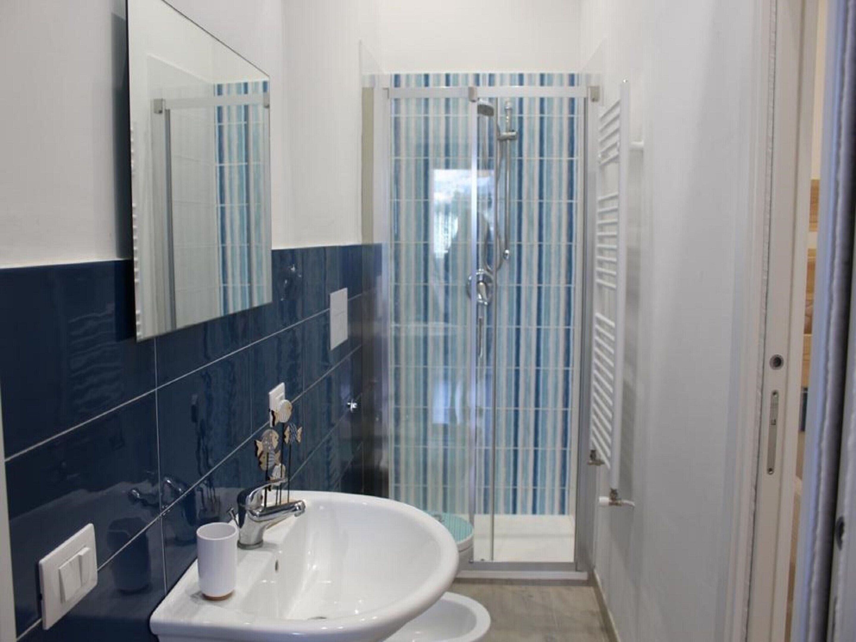 Un baño con lavamanos blanco, espejo y ducha con puerta de cristal.