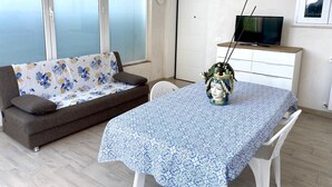 A living room with a sofa, a dining table, a TV, and a decorative vase. - Villa in Sicily With Sea Access (Santa Flavia)