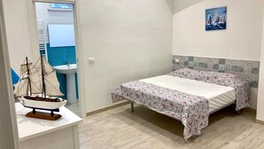 A bedroom with a bed, a small table with a ship model, a painting, and a bathroom visible through an open door. - Villa in Sicily With Sea Access (Santa Flavia)