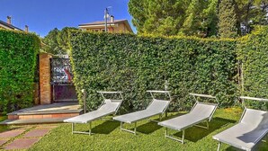 A garden with four sun loungers, a hedge, and a building in the background. - Belvilla by OYO Villa Trecastagni (Trecastagni)