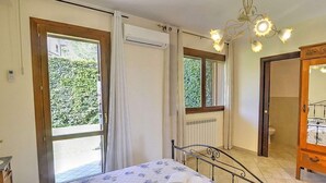 A bedroom with a bed, a window, an air conditioning unit, a chandelier, and a wooden wardrobe. - Belvilla by OYO Villa Trecastagni (Trecastagni)