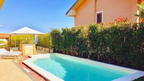 A swimming pool with lounge chairs and a covered area, surrounded by a hedge and a building. - Belvilla by OYO Villa Trecastagni (Trecastagni)
