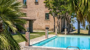 A building with a pool, surrounded by palm trees and a clear view of the sea. - Lavish Sicilian Villa With Pool (Ficarra)