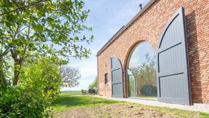 A brick building with large arched windows and doors, surrounded by greenery and a grassy area.