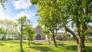 A brick building with a large arched entrance, surrounded by a grassy field and trees.