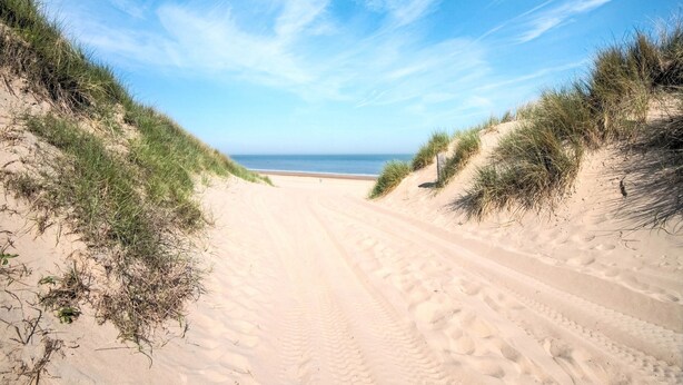 A sandy beach path leading to the sea, surrounded by grassy dunes.