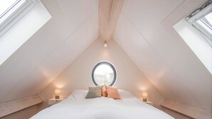 A bedroom with a sloped ceiling, a round window, and two bedside lamps.