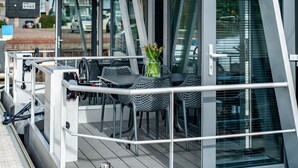 Une terrasse extérieure moderne, dotée de rampes en métal, d’une table avec des chaises et d’une porte vitrée donnant sur l’intérieur.