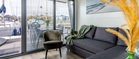 A modern living room with a sofa, a chair, and a large window overlooking a marina.
