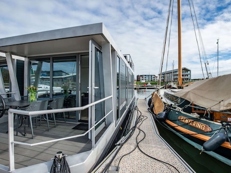 A modern boat with a covered deck area, glass windows, and outdoor seating.