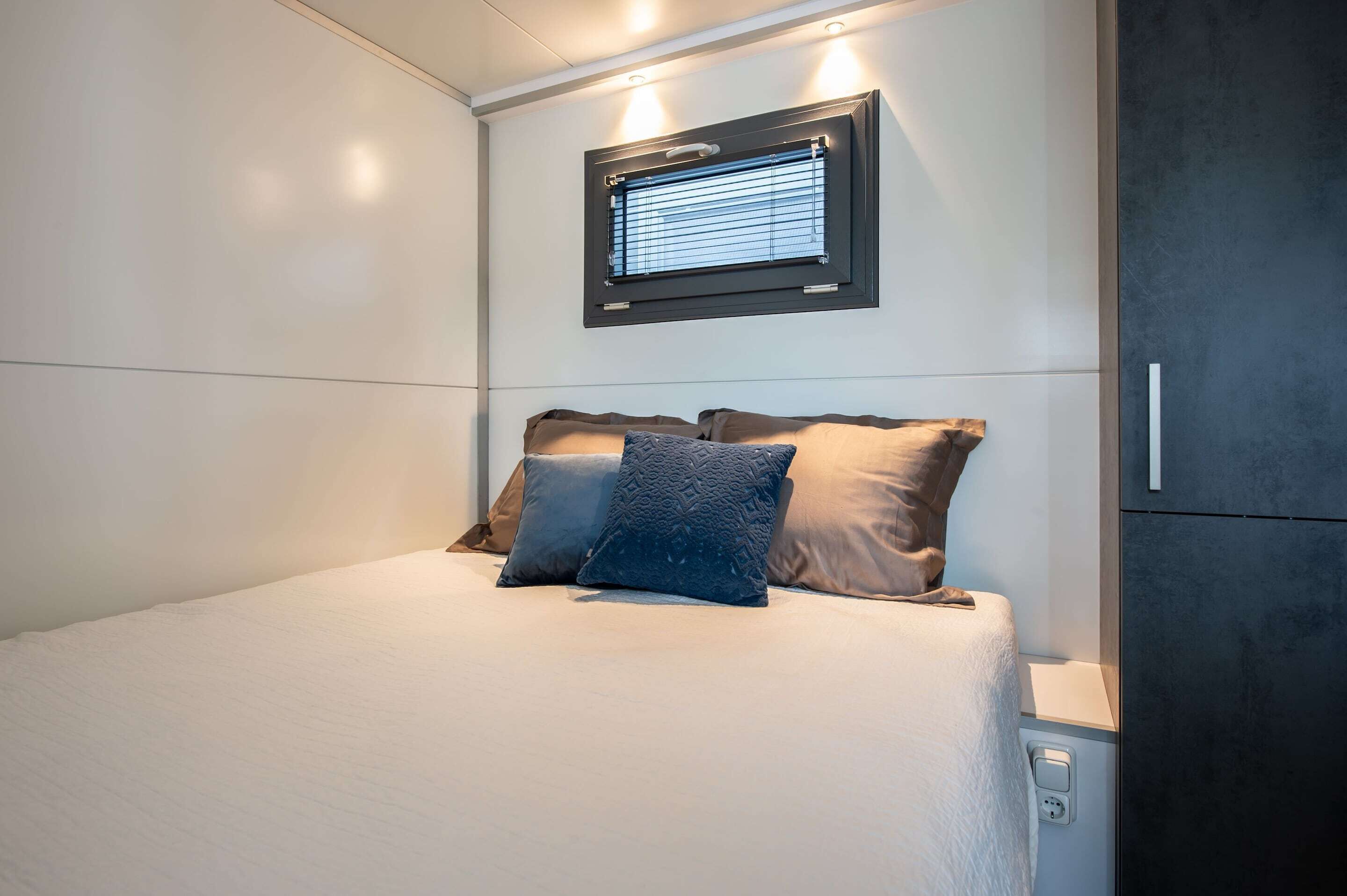 Une chambre moderne avec un lit, des oreillers, une fenêtre et un luminaire fixé au mur.