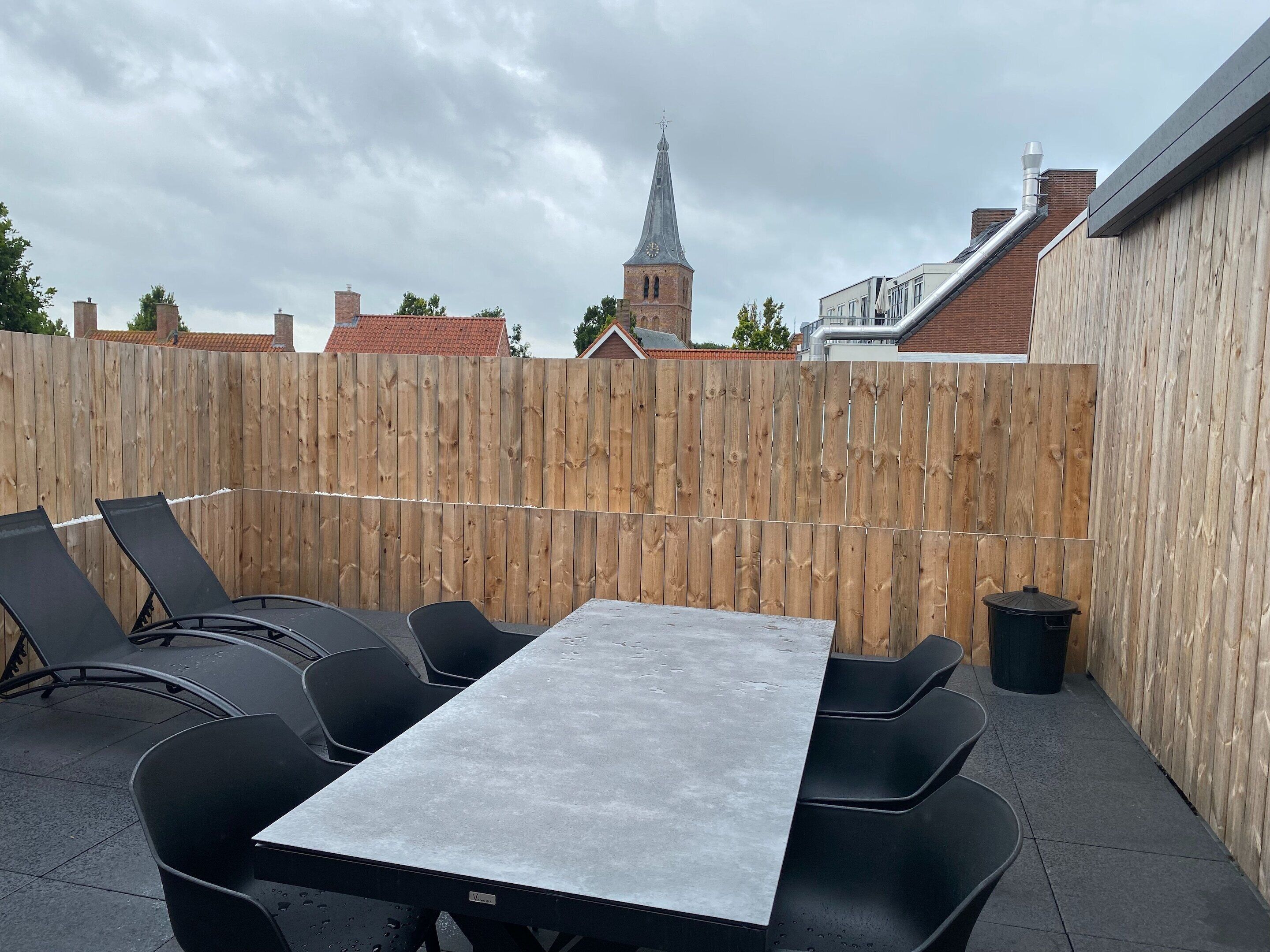 A patio with a table and chairs, a wooden fence, and a view of a church tower.