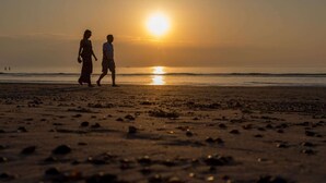 Une scène de plage où deux personnes marchent en direction du coucher de soleil.