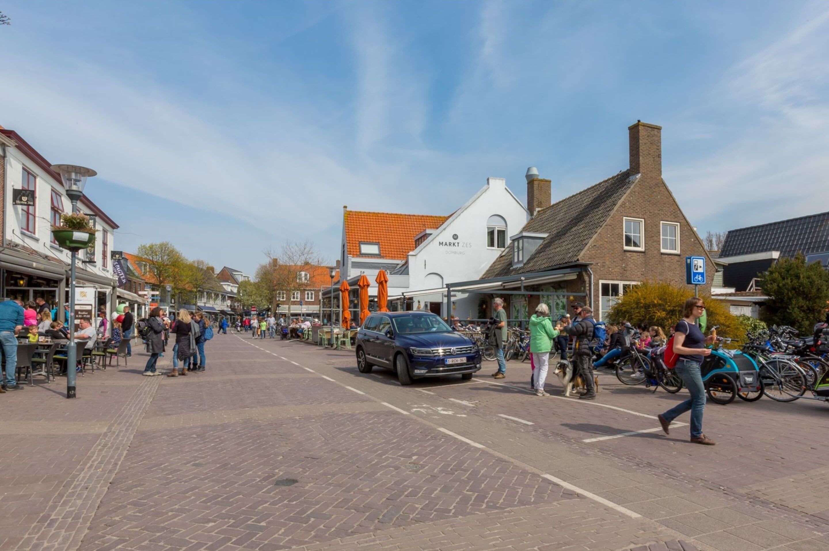 A bustling street scene with pedestrians, bicycles, and parked cars.