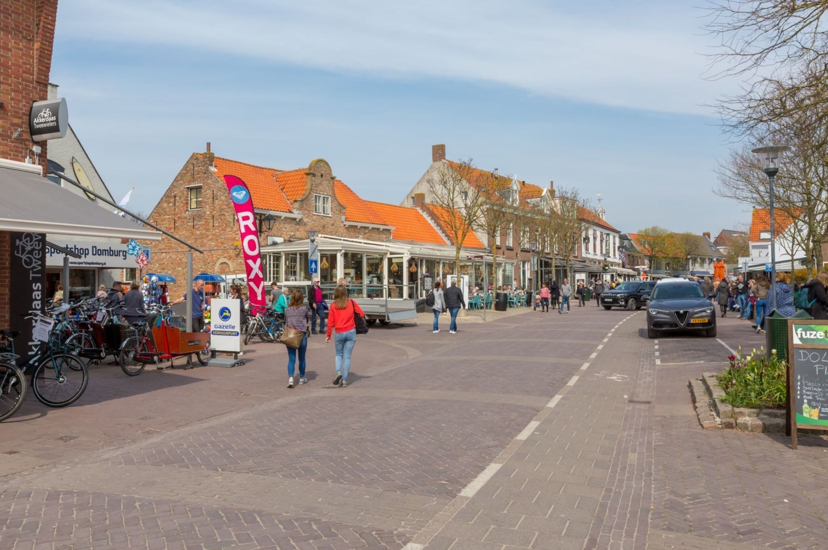 A street scene with a row of buildings, a bicycle parking area, and people walking.