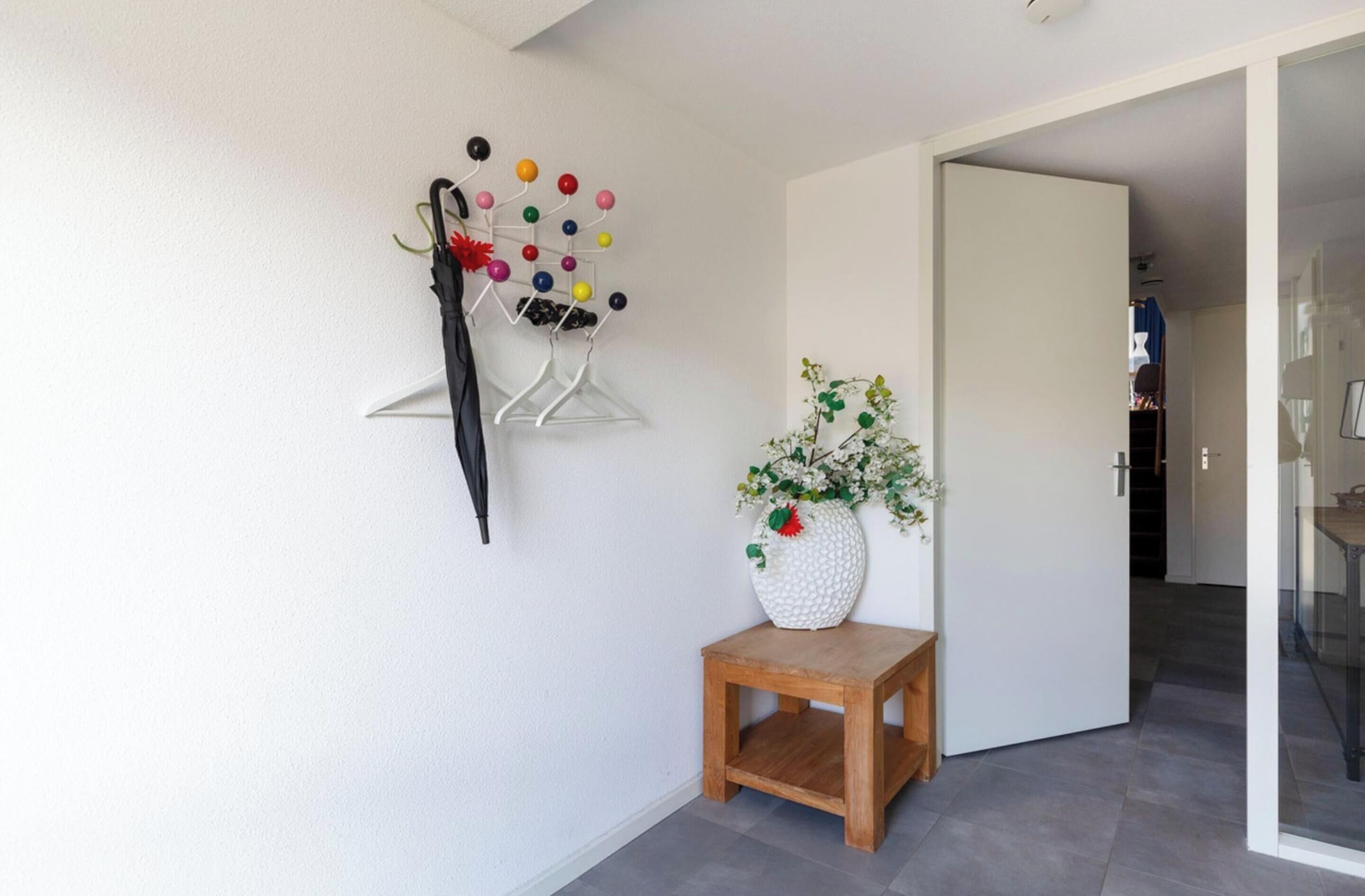 A hallway with a wall-mounted rack holding colorful balls, a black umbrella, and a small wooden table with a white vase of flowers.