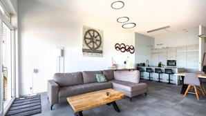 A modern living room with a sofa, coffee table, and a kitchen in the background. - Spacious Flat With Views of the Harbour (Ouddorp)