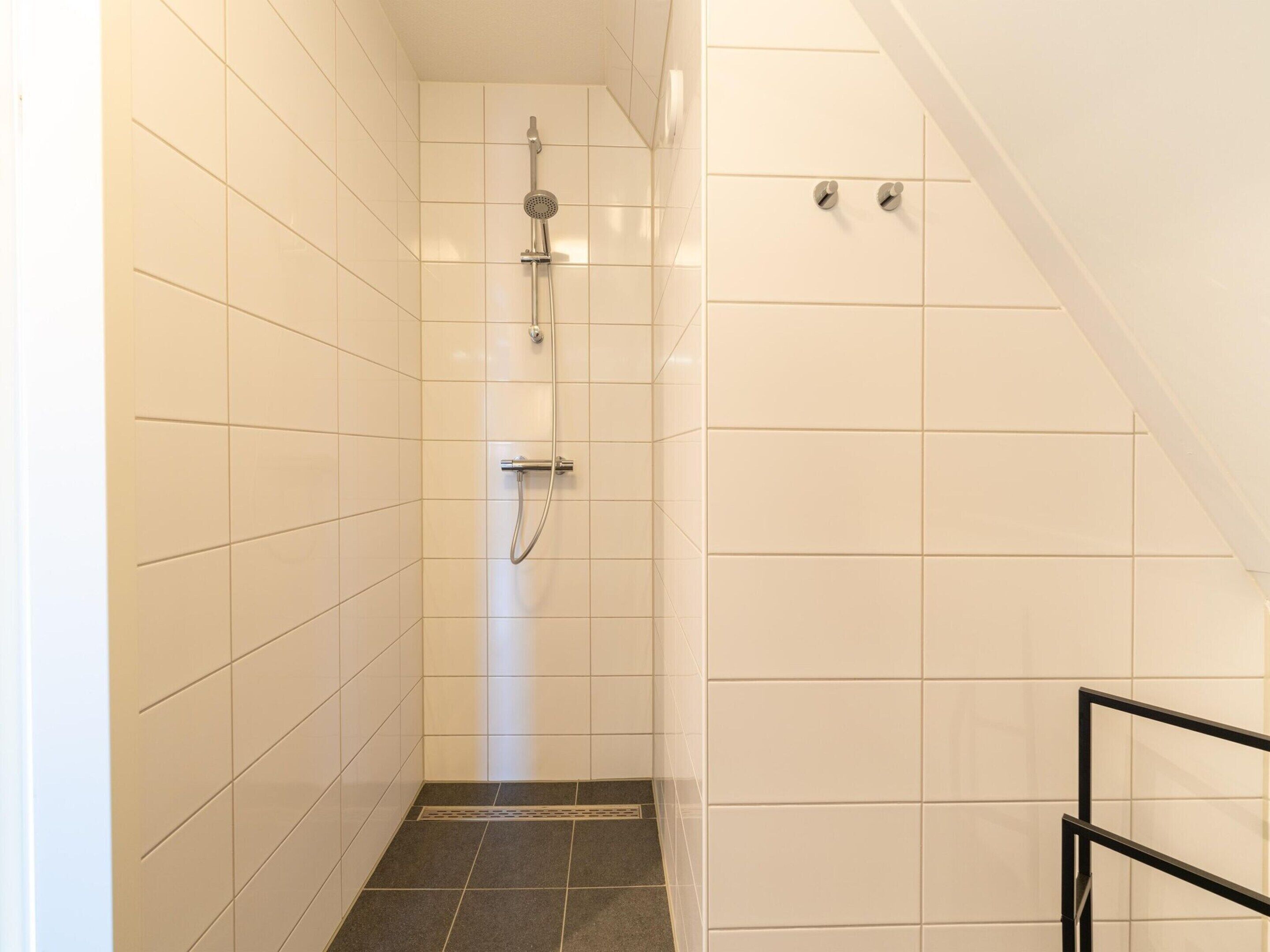 A narrow shower area with white tiled walls and a dark tiled floor.