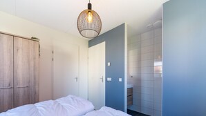 Quarto com duas camas, um guarda-roupa, banheiro com pia e espelho, e luminária suspensa.