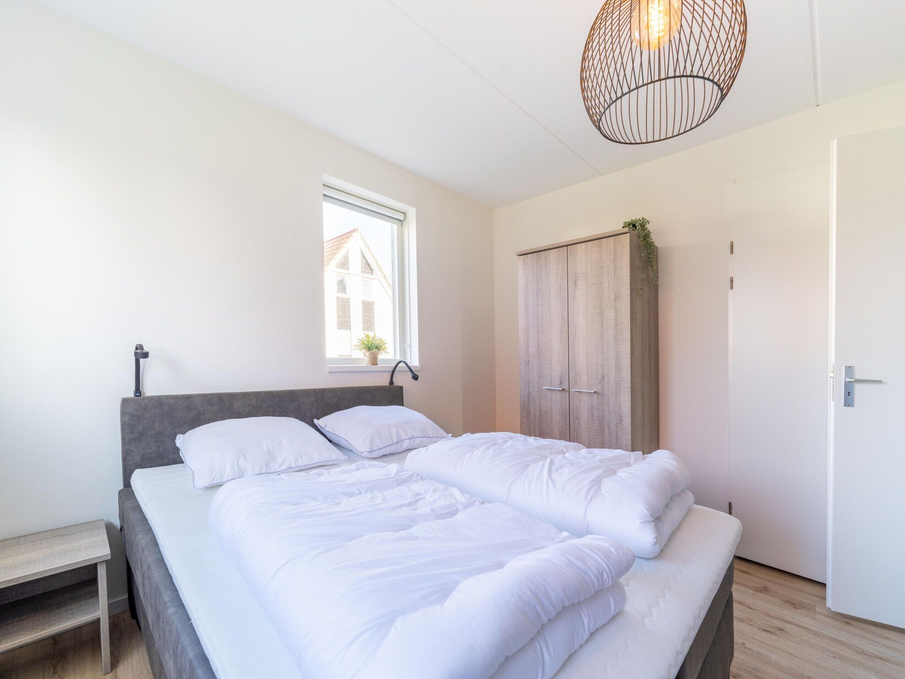 A bedroom with a bed, a window, a wardrobe, and a hanging light fixture.