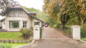 Een twee verdiepingen tellend huis met een geplaveid pad dat leidt naar een toegangshek.