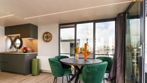 Eine moderne Küche mit einem runden Esstisch, grünen Stühlen und Blick auf die Stadt durch große Fenster.