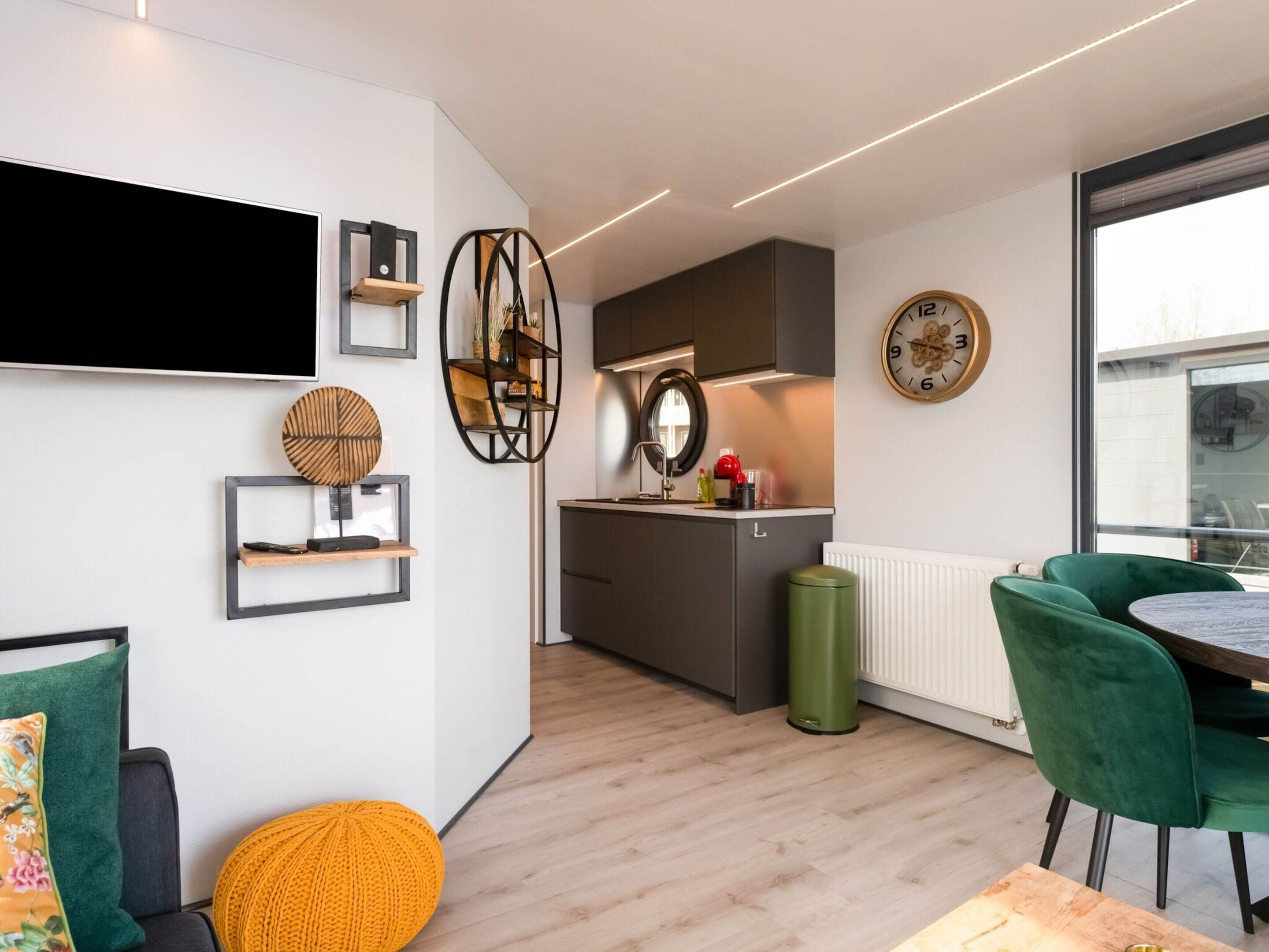 Een moderne keuken met een ingebouwde oven, een groene prullenbak en een eethoek met een ronde tafel en groene stoelen.