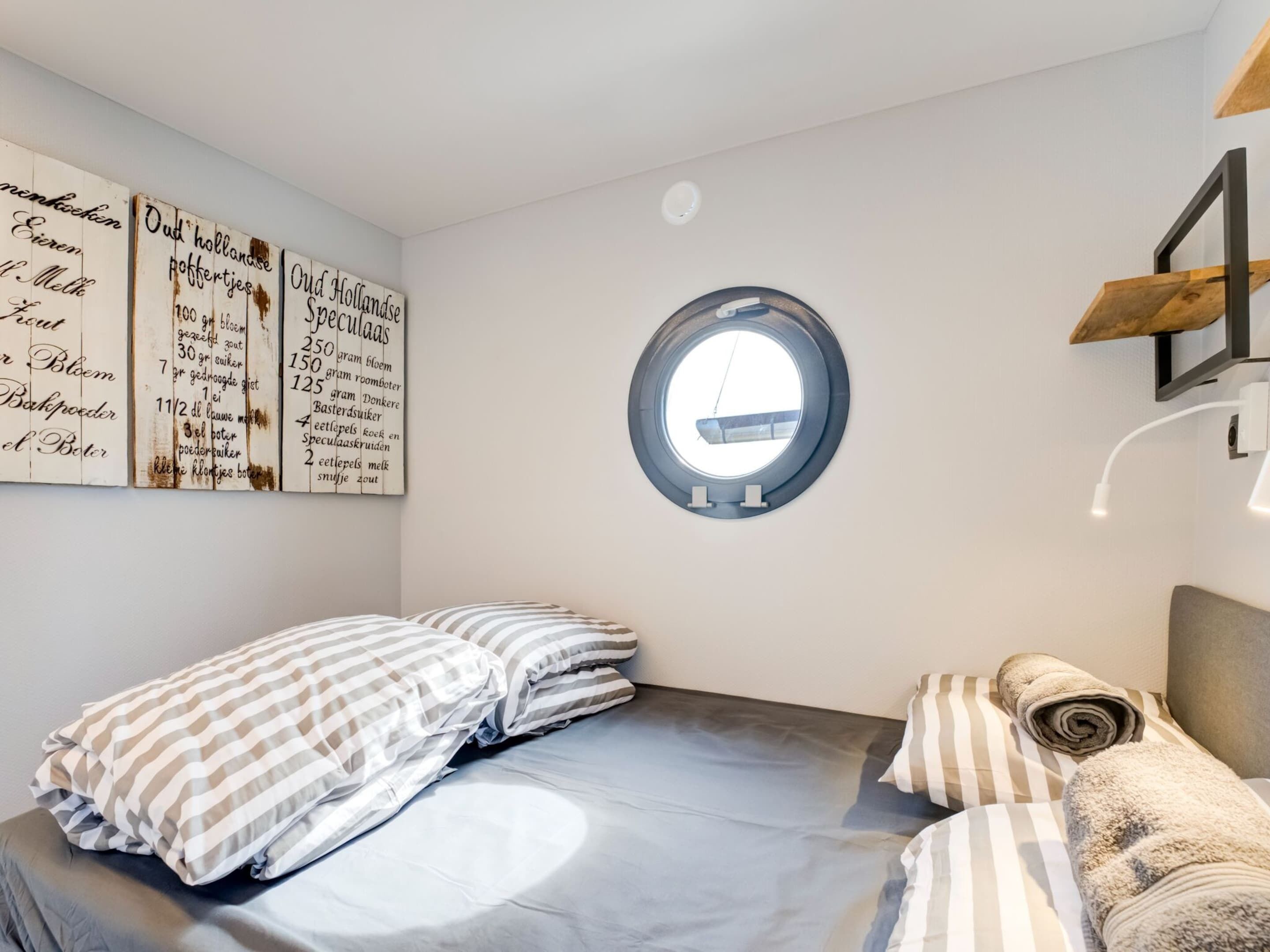 Quarto com cama, almofadas, janela redonda e parede com texto.