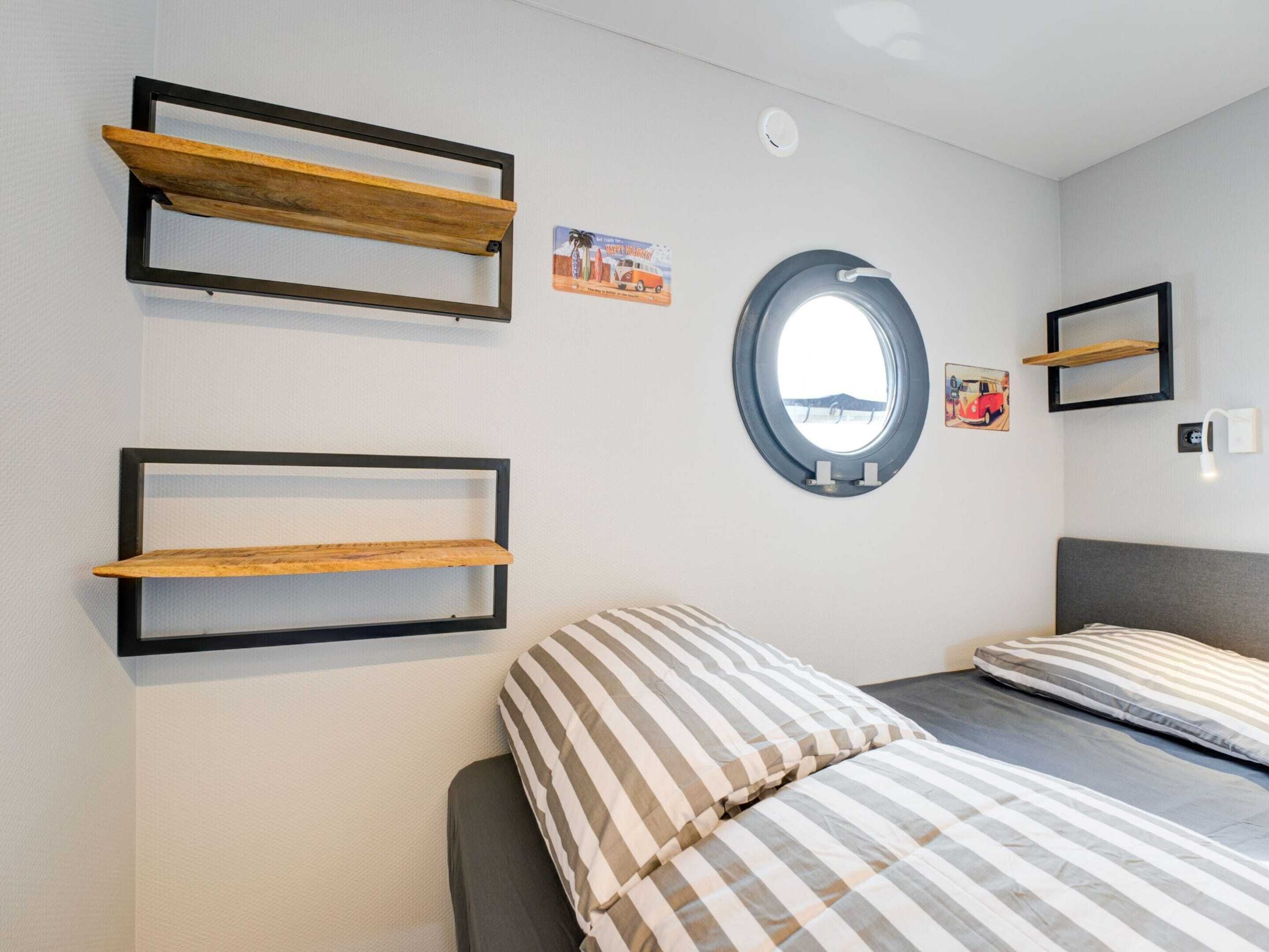 A bedroom with two wooden shelves, a round mirror, and a bed with striped bedding.