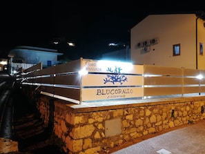 A stone wall with a sign for 'Casa Vacanze BLUCORALLO' and a contact number.